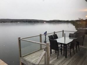Une terrasse en bois avec une rambarde en verre, donnant sur un lac paisible, le tout entouré de collines.