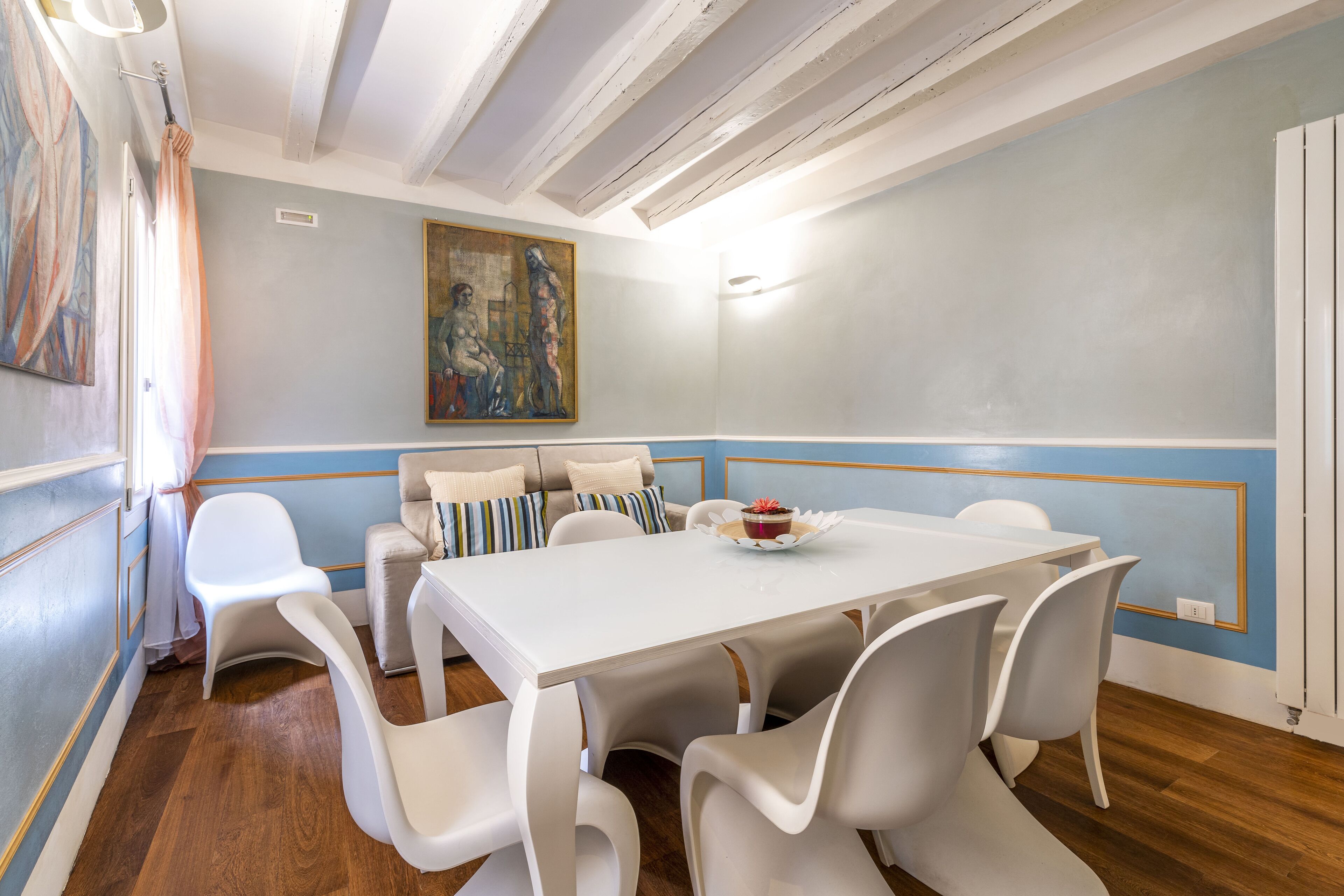 A dining area with a white table, white chairs, and a painting on the wall.