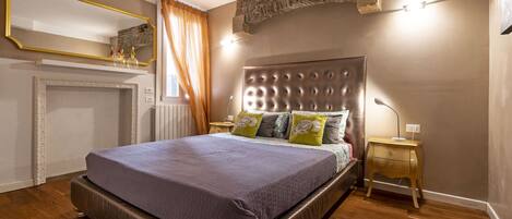 A bedroom with a large bed, a wooden nightstand, a mirror, and a stone accent wall.