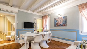 Un área de comedor con una mesa y sillas blancas, un televisor y un cuadro en la pared.