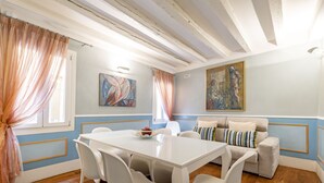 Un área de comedor con una mesa y sillas blancas, un sofá con cojines y obras de arte en las paredes.