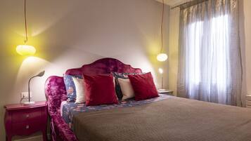 Une chambre à coucher avec un grand lit, une table de chevet, une lampe et une fenêtre avec des rideaux.