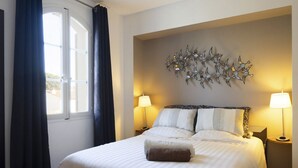 A hotel room with a bed, two bedside lamps, a decorative wall piece, and a window with curtains. - Superb Fisherman's House with Private Pool / Mooring - Port Grimaud (Grimaud)