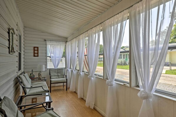 A room with a row of chairs, a table, and large windows with white curtains.