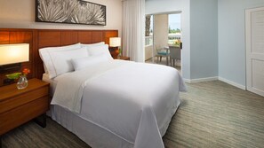 Quarto de hotel com uma cama grande, cabeceira de madeira, duas mesas de cabeceira com luminárias, um vaso com flores e vista para a varanda.