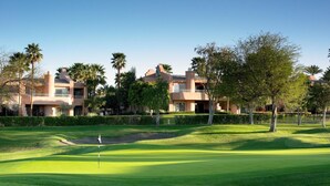 Un terrain de golf avec un mât de drapeau, une pelouse parfaitement entretenue et, au fond, un bâtiment doté de plusieurs balcons.