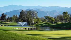 Un parcours de golf avec un étang, des arbres et des montagnes en arrière-plan.