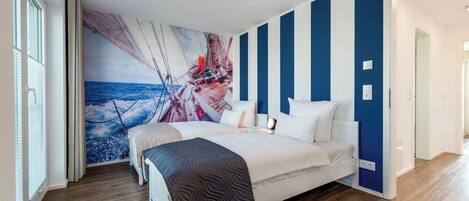 A bedroom with a large bed, a nautical-themed wall mural, and a view of the ocean through the window.
