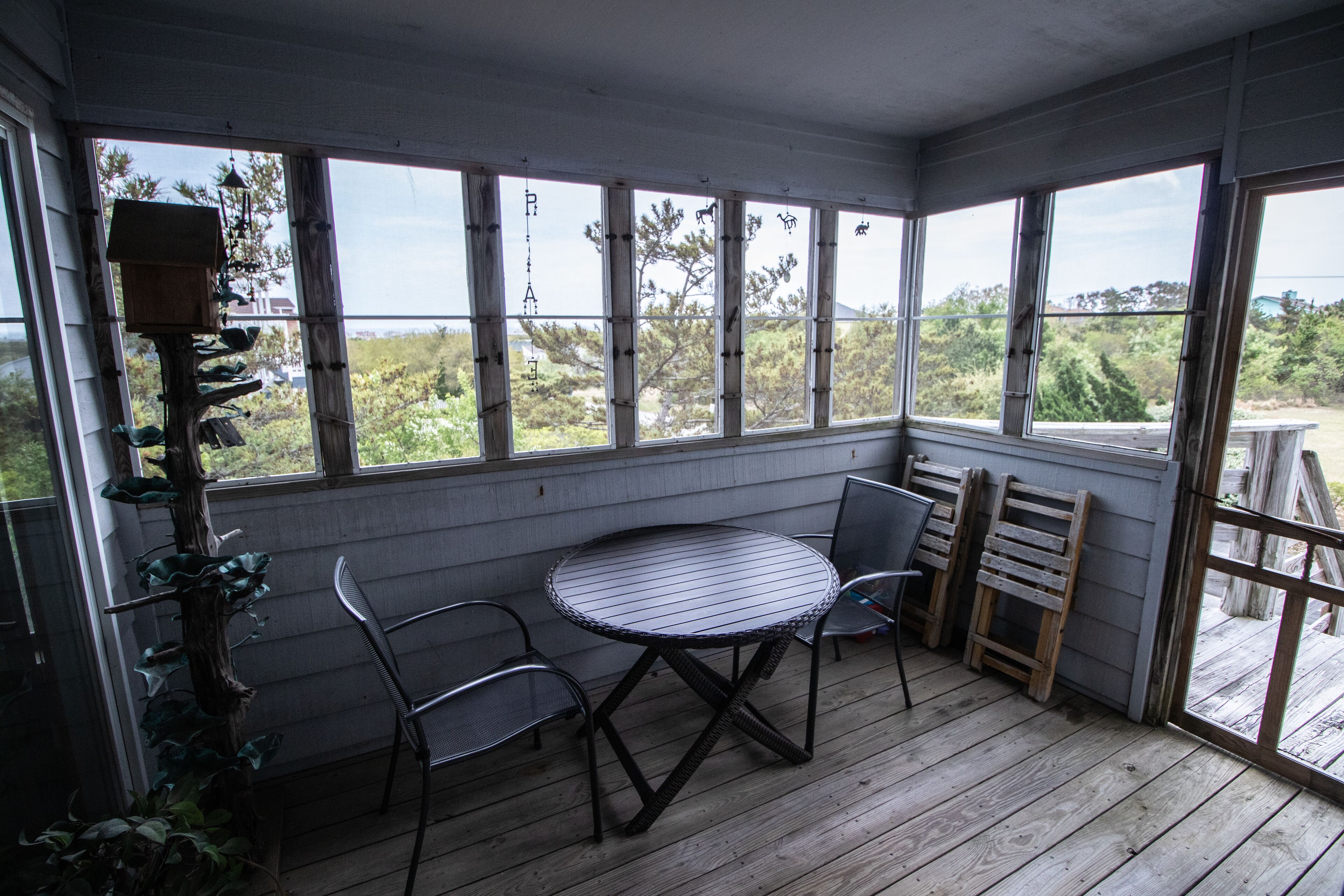 A covered patio with a round table and two chairs, large windows, and a birdhouse.