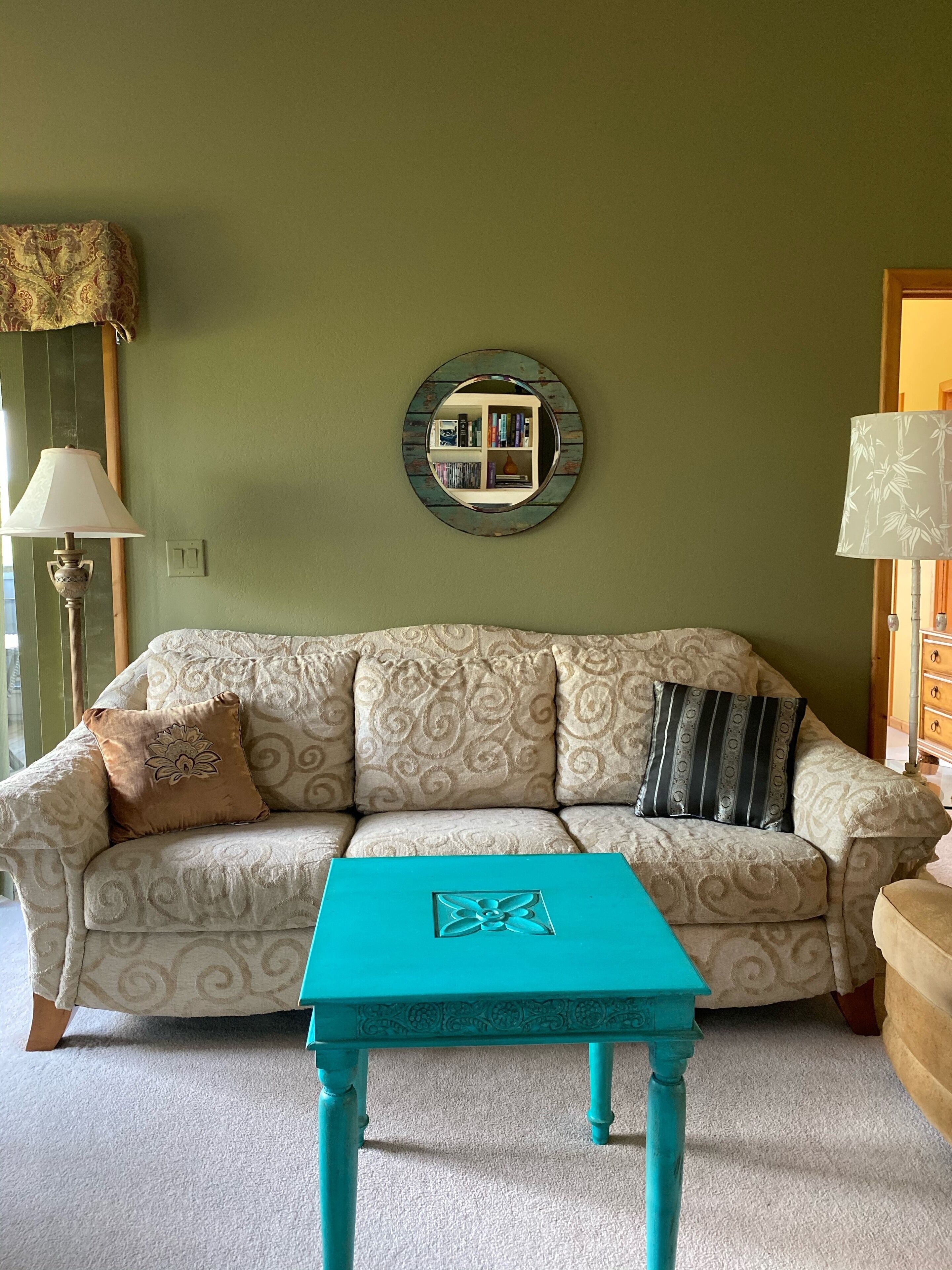 A living room with a patterned sofa, a turquoise coffee table, and a mirror on the wall.