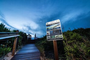 A wooden boardwalk leading to a beach area with a sign about sea turtle nesting season.