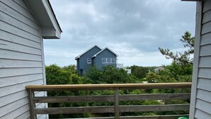 Une terrasse en bois avec deux chaises et une rambarde, d’où l’on a vue sur une maison et la verdure environnante.