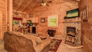 Interior acogedor de una cabaña con chimenea, televisor, sofá y zona de cocina.