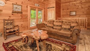 Interior acogedor de una cabaña de troncos con un sofá de cuero marrón, una mesa de centro de madera y una alfombra estampada.