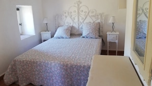 Un dormitorio con una cama, dos mesitas de noche, un ventanal y un espejo.