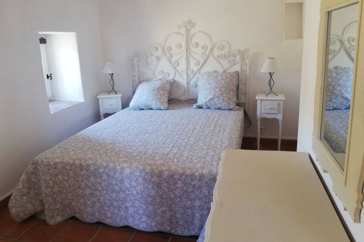 A bedroom with a bed, two bedside tables, a window, and a mirror.
