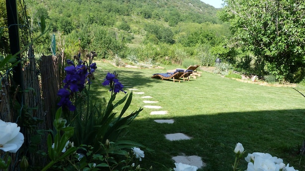Un jardín con rosas blancas, flores moradas y césped con tumbonas.
