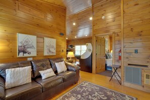 Un intérieur en bois avec un canapé en cuir, des œuvres d’art encadrées, une lampe et une cheminée.