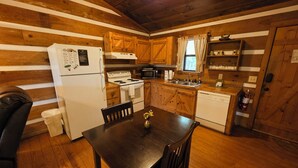 A cabin-style kitchen with wooden walls, a stove, refrigerator, and a dining table with chairs. - McKenzie Cabin: A Cozy Romantic Updated Retreat with Mountain Views and Hot Tub (Sevierville)