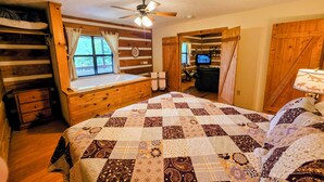 A log cabin bedroom with a large bed, a wooden dresser, a window with curtains, a ceiling fan, and a television in the corner. - McKenzie Cabin: A Cozy Romantic Updated Retreat with Mountain Views and Hot Tub (Sevierville)
