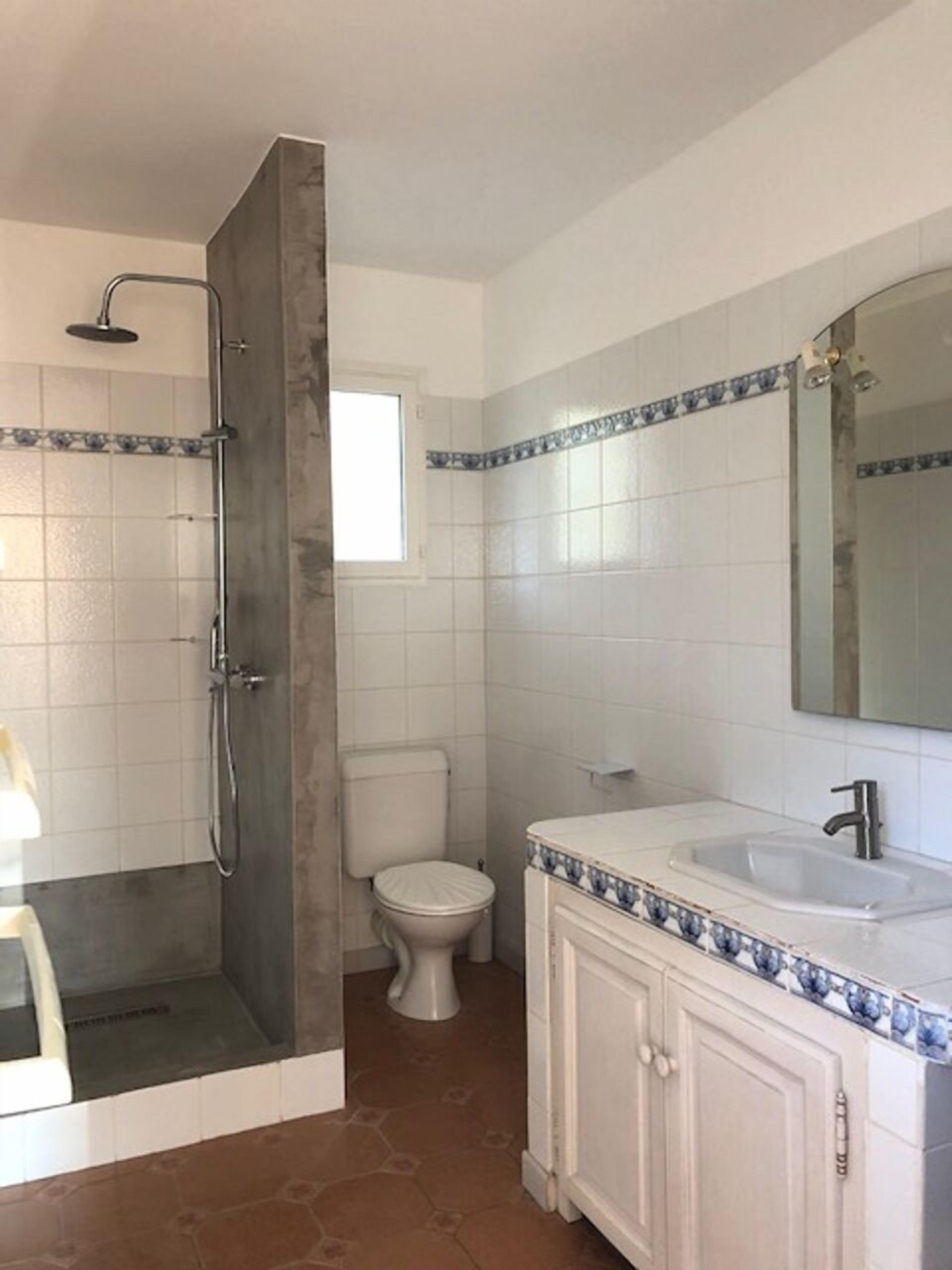 Casa de banho com chuveiro, sanita, lavatório e espelho.