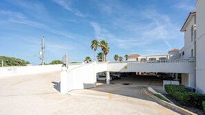 A white building with a covered parking area and a pedestrian bridge.