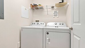 Ein Waschraum mit zwei Whirlpool Waschmaschinen und Trocknern, einem Metallregal mit Waschmitteln und einem Schild, das darauf hinweist, Handtücher vor dem Waschen auszuschütteln.