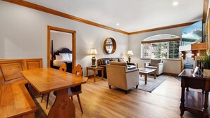 A cozy living room with a wooden dining table, a sofa, and a large window offering a view of a mountain. - 3 Bedroom~Heated Pool, Tubing & Ice Skating Villa 2082-3 (Midway)