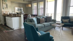 Un salon spacieux avec un canapé de couleur turquoise, une table basse et un coin repas, la cuisine étant visible au fond.