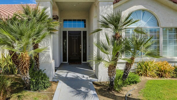 A two-story house with a tiled roof, a front door with glass panels, and a large arched window. - Palm Desert Oasis For The Whole Family To Enjoy (Palm Desert)
