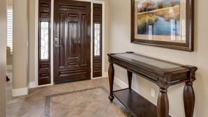 A hallway with a dark wooden double door, a glass-top console table, and a framed landscape painting on the wall. - Palm Desert Oasis For The Whole Family To Enjoy (Palm Desert)