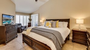 A bedroom with a bed, two bedside tables, a ceiling fan, a TV on a dresser, and a window with blinds. - Palm Desert Oasis For The Whole Family To Enjoy (Palm Desert)
