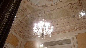 Una habitación con candelabro, techo ornamentado y una puerta con interruptor de luz.