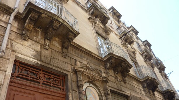 Un edificio histórico con detalles arquitectónicos ornamentales, incluyendo una puerta de madera grande, herrajes decorativos y un mural.