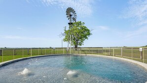 Une piscine avec un moulin à vent et un arbre au centre, le tout entouré d’une clôture.