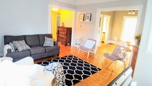 A living room with a grey sofa, patterned cushions, a black and white rug, a small white table, and a grey armchair. - Beside The Tulip Tree - 3Bd Historic Home located in Waterfront District (Shelburne)