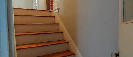 A wooden staircase with white walls and a door at the bottom.