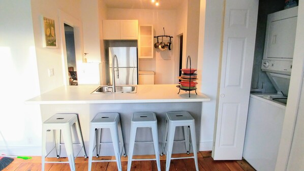 A kitchen with a white countertop, stainless steel appliances, and a hanging pot rack. - Beside The Tulip Tree - 3Bd Historic Home located in Waterfront District (Shelburne)