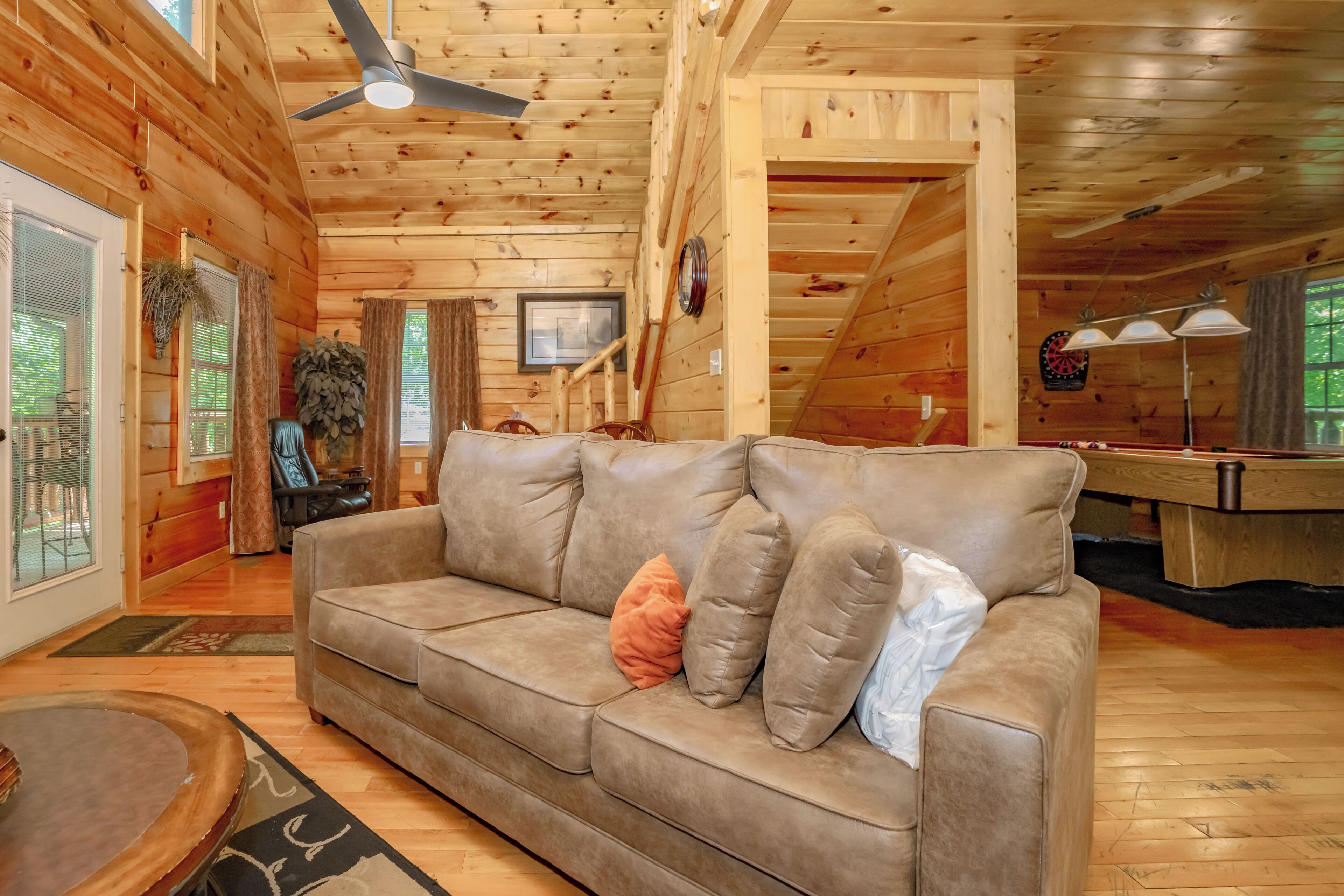 A wooden interior with a sofa, ceiling fan, and a dartboard.