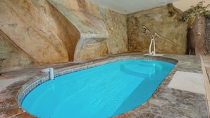 Una piscina interior con borde de azulejos, pared de roca y escultura de árbol.
