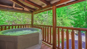 Una terraza de madera con un jacuzzi y vistas a un bosque.