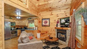 Interior de una cabaña de madera con sala de estar, cocina y chimenea.