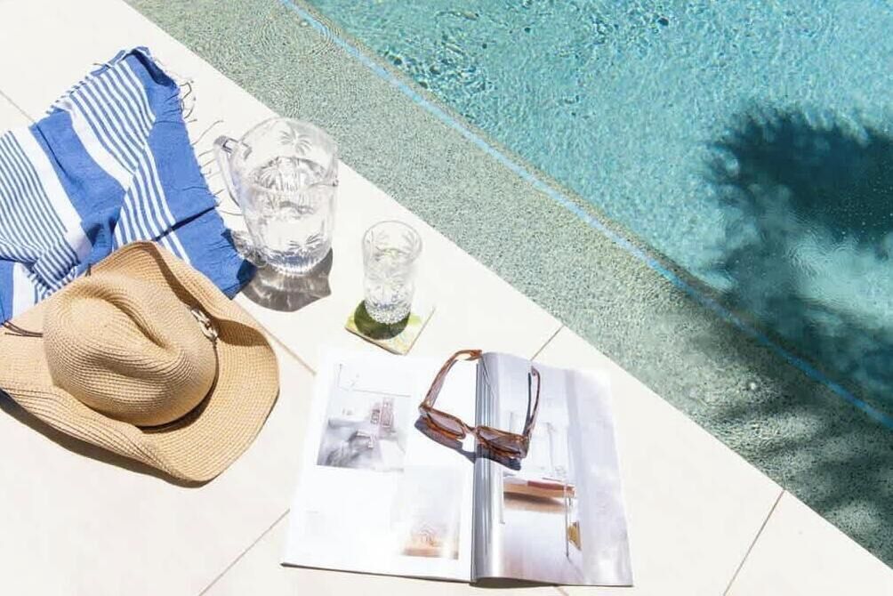 A poolside setting with a hat, sunglasses, a striped towel, and a glass.