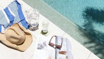 A poolside setting with a hat, sunglasses, a striped towel, and a glass.