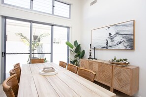 Un coin repas avec une table en bois, des chaises en osier, un buffet et une grande fenêtre donnant sur un paysage verdoyant.