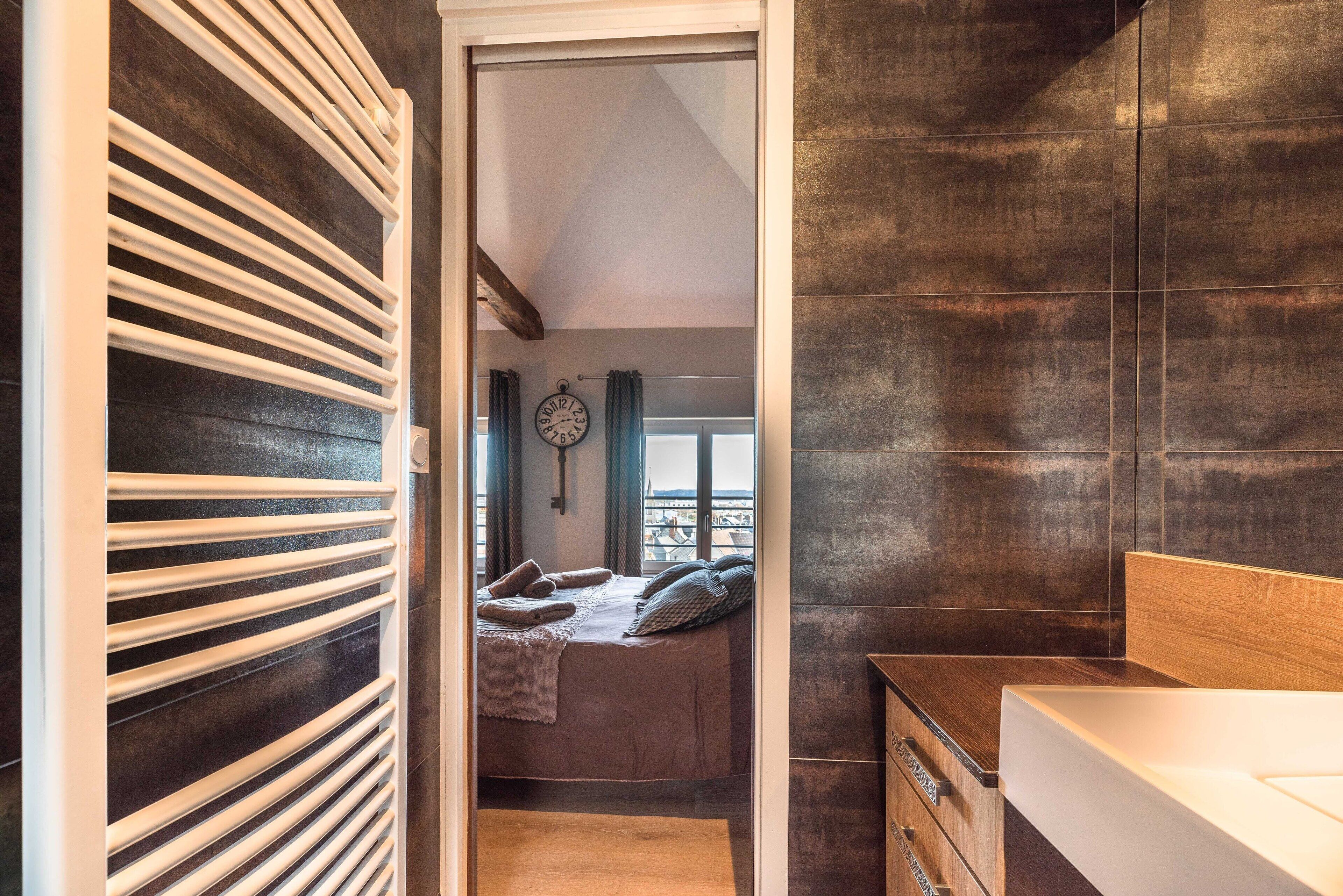 Une chambre à coucher moderne avec un lit, une tête de lit en bois, une table de chevet et une grande fenêtre avec des rideaux.
