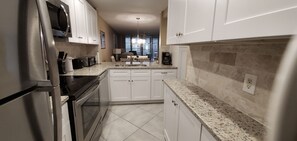 A modern kitchen with white cabinets, granite countertops, a stainless steel refrigerator, and a built-in oven.