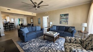 A spacious living room with a large blue sofa, a patterned rug, and a ceiling fan.