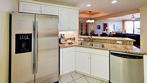 A modern kitchen with white cabinets, a stainless steel refrigerator, a dishwasher, and a granite countertop.