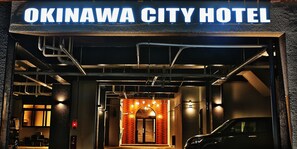 The exterior of the Okinawa City Hotel with a prominent sign, a modern entrance, and a parked car. - Okinawa City Hotel (Okinawa)